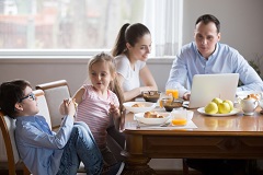 Family at dinner table, parents looking at tax changes on a laptop